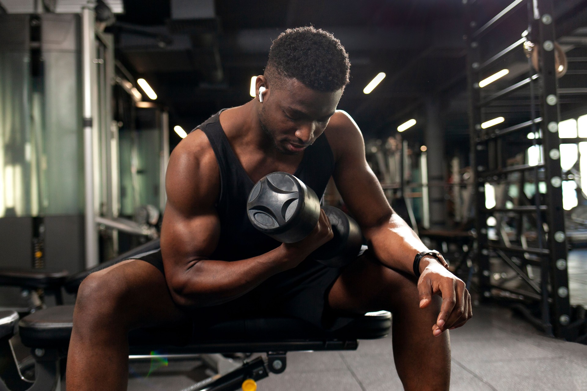 athletic african american man trains in dark gym, athletic guy lifts heavy dumbbells in fitness club